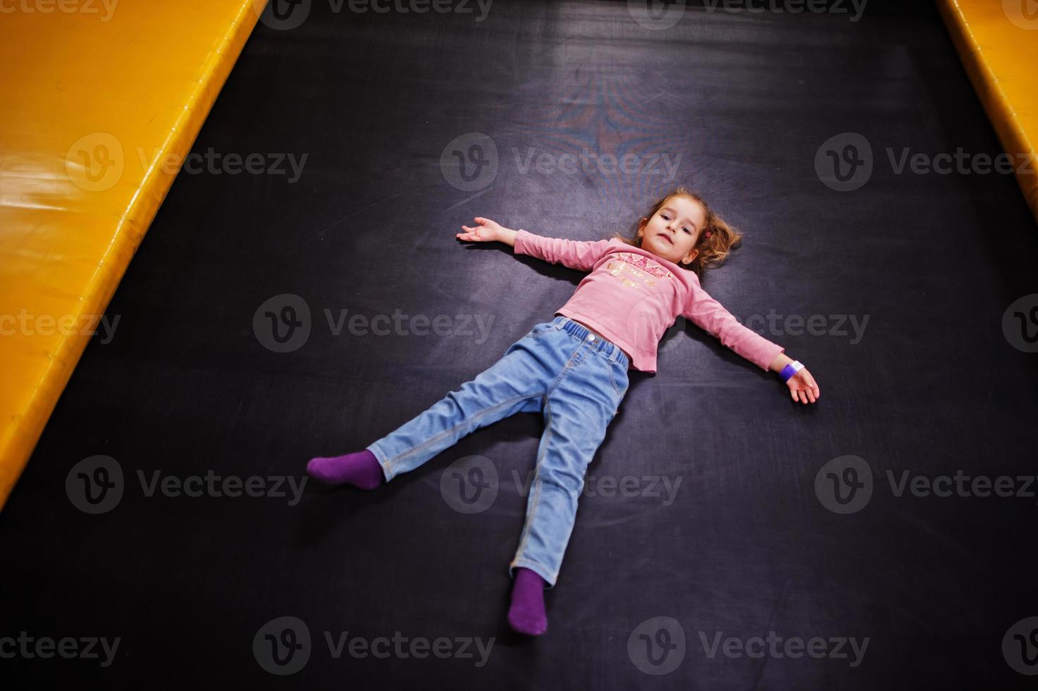 jolie petite fille allongée sur un trampoline dans un centre de jeux intérieur. photo