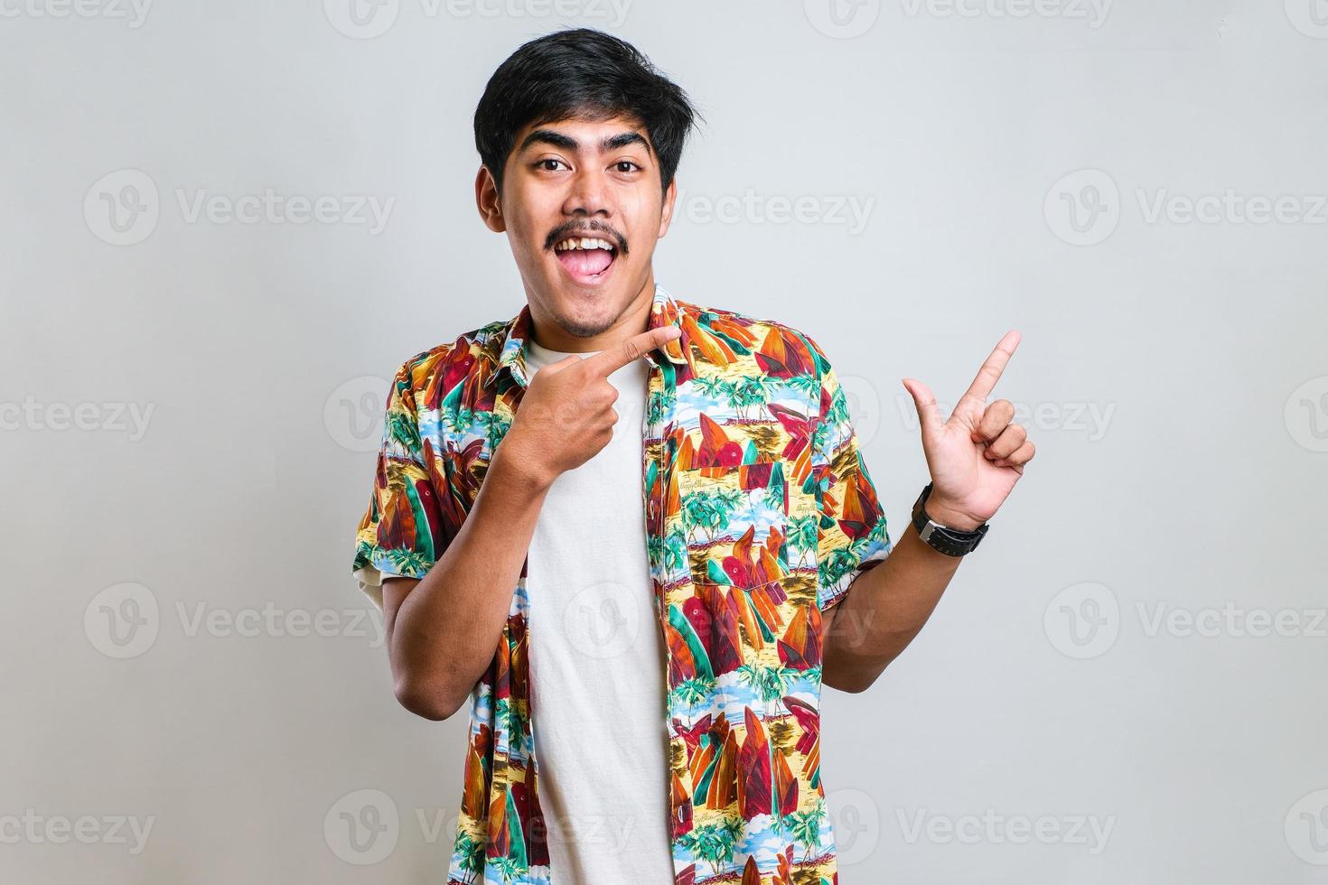 homme asiatique avec un grand sourire sur le visage, pointant avec le doigt de la main sur le côté en regardant la caméra. photo