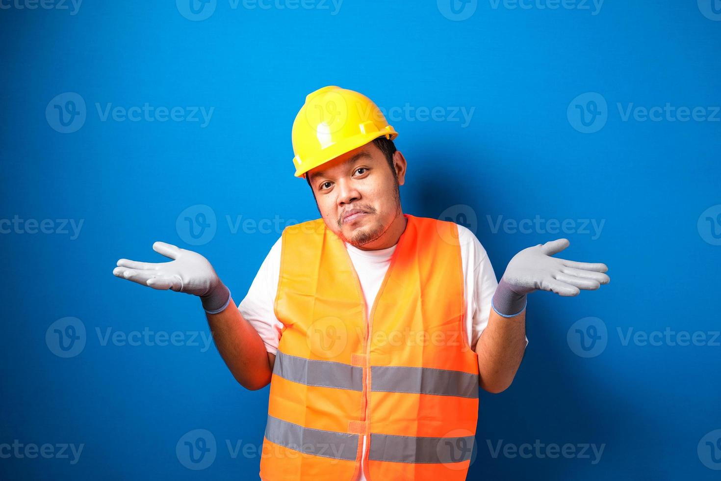 jeune beau gros travailleur asiatique homme portant un uniforme de gilet de sécurité orange et un casque expression désemparée et confuse avec les bras et les mains levés photo