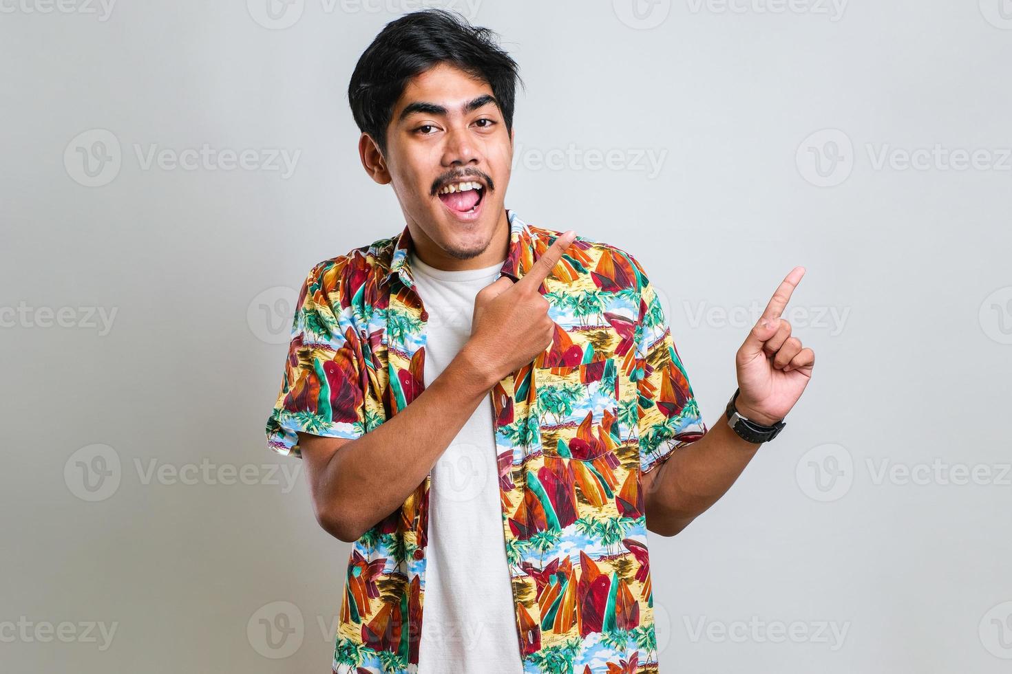 homme asiatique avec un grand sourire sur le visage, pointant avec le doigt de la main sur le côté en regardant la caméra. photo