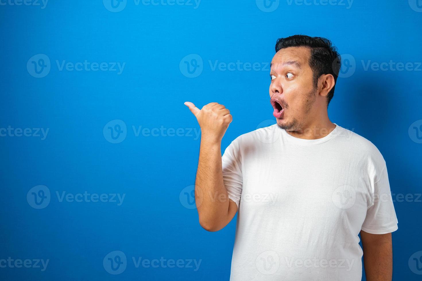 gros homme asiatique en t-shirt blanc montre une drôle d'expression choquée et surprise sur fond bleu photo