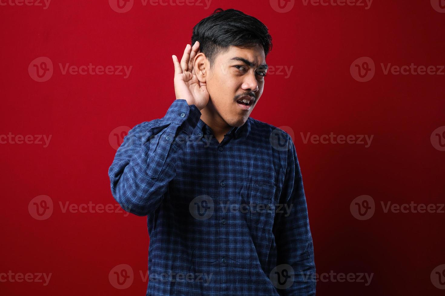 jeune bel homme asiatique portant une chemise décontractée curieux avec la main sur l'oreille écoutant une rumeur ou des commérages. notion de surdité. photo