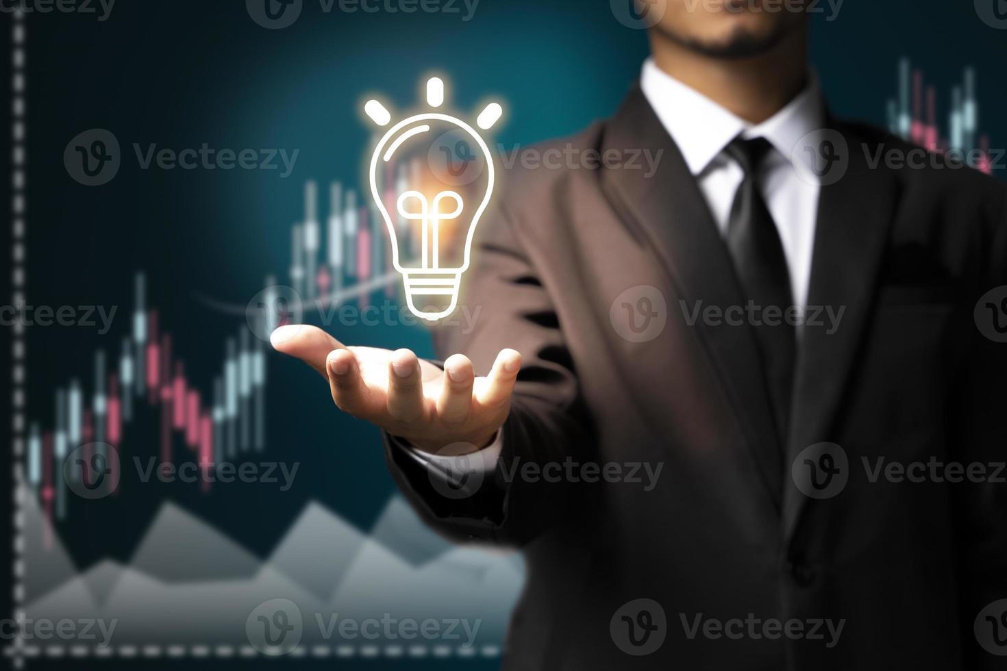 un homme d'affaires dans le commerce d'idées montre une icône de lampe avec un stock d'hologrammes virtuels croissant, investissez dans le commerce. photo
