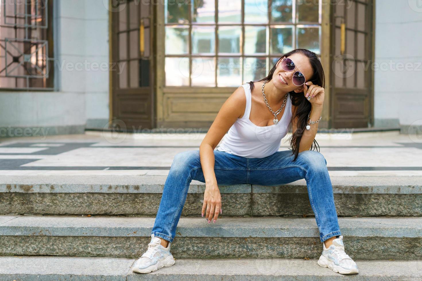 style décontracté. femme élégante à lunettes de soleil assis sur un escalier en pierre. elle était photo