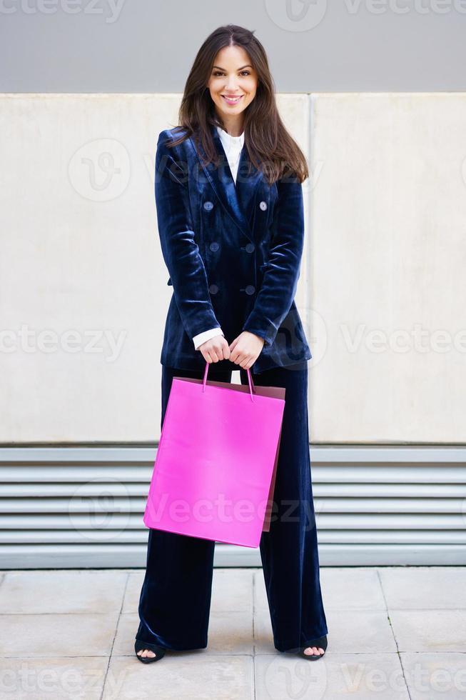 jeune femme portant un costume bleu transportant plusieurs sacs à provisions près d'un centre commercial. photo