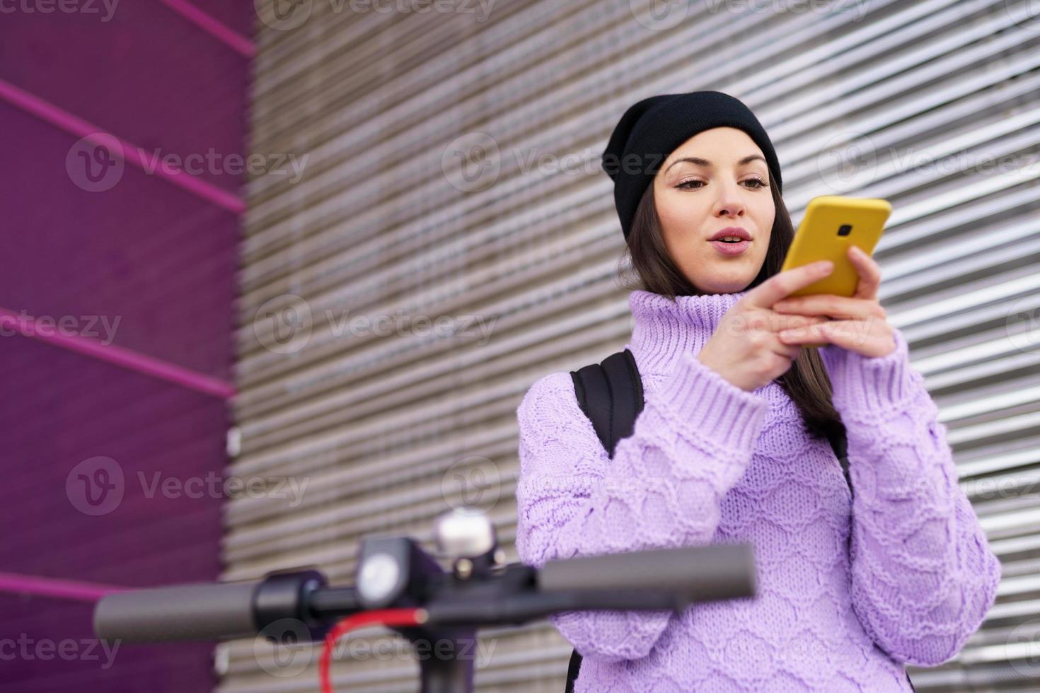 femme dans la vingtaine avec scooter électrique enregistrant une note vocale avec un smartphone à l'extérieur. photo