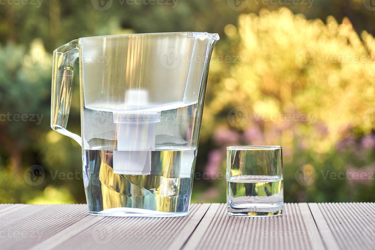 pichet de filtre à eau et un verre propre d'une eau claire gros plan sur le fond du jardin d'été photo