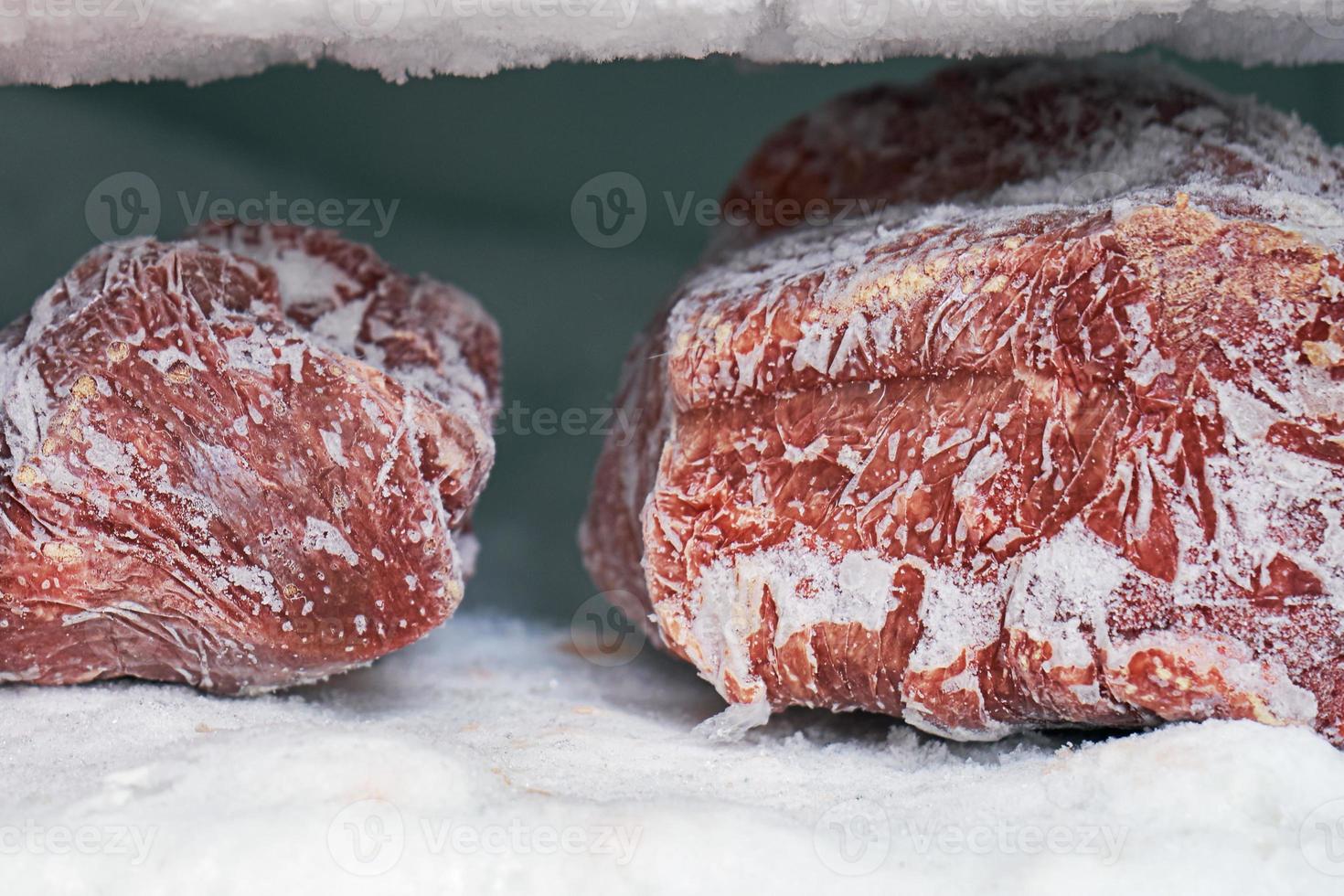 gros morceaux de viande rouge dans un congélateur avec une grande quantité de glace et de neige congelées photo