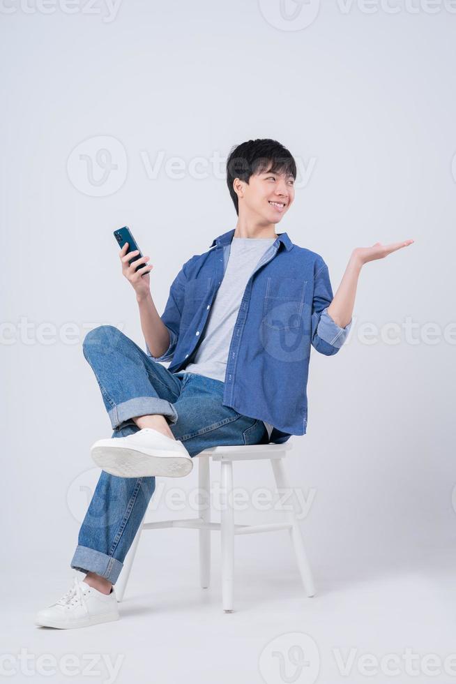 jeune homme asiatique assis et utilisant un smartphone sur fond blanc photo