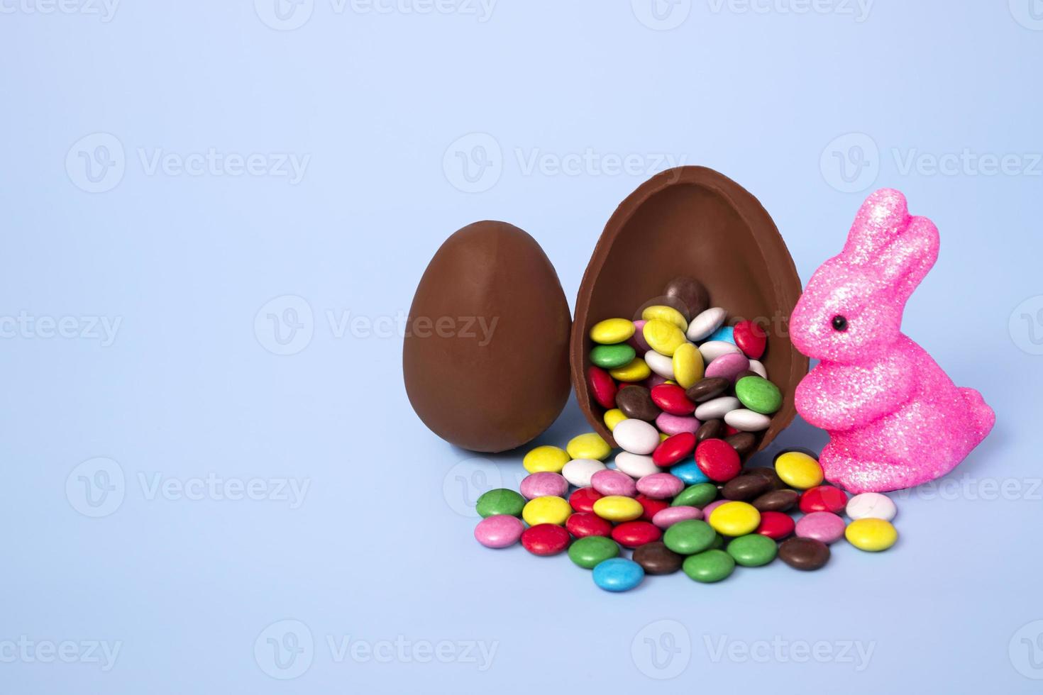 oeuf en chocolat avec des bonbons colorés et un lapin sur fond bleu. bannière festive avec espace de copie. photo