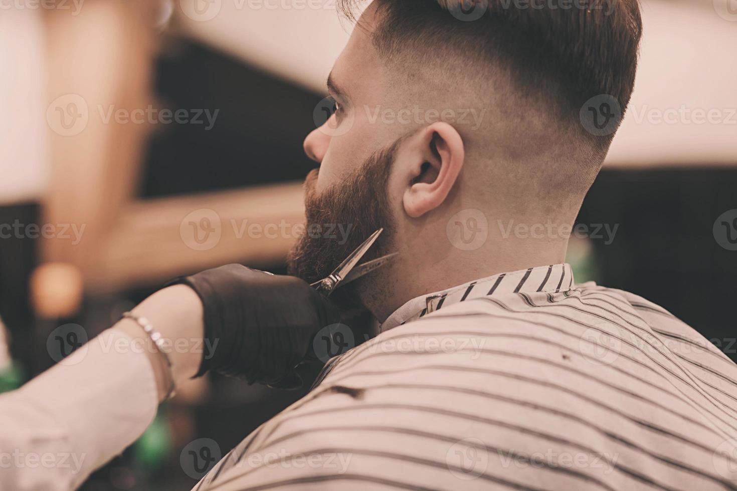 le coiffeur coupe la barbe de l'homme photo