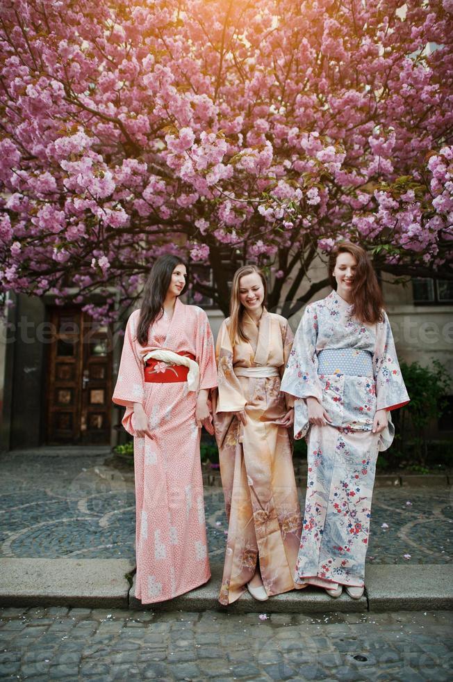 trois filles européennes portant un kimono japonais traditionnel fond arbre de sakura rose fleur photo