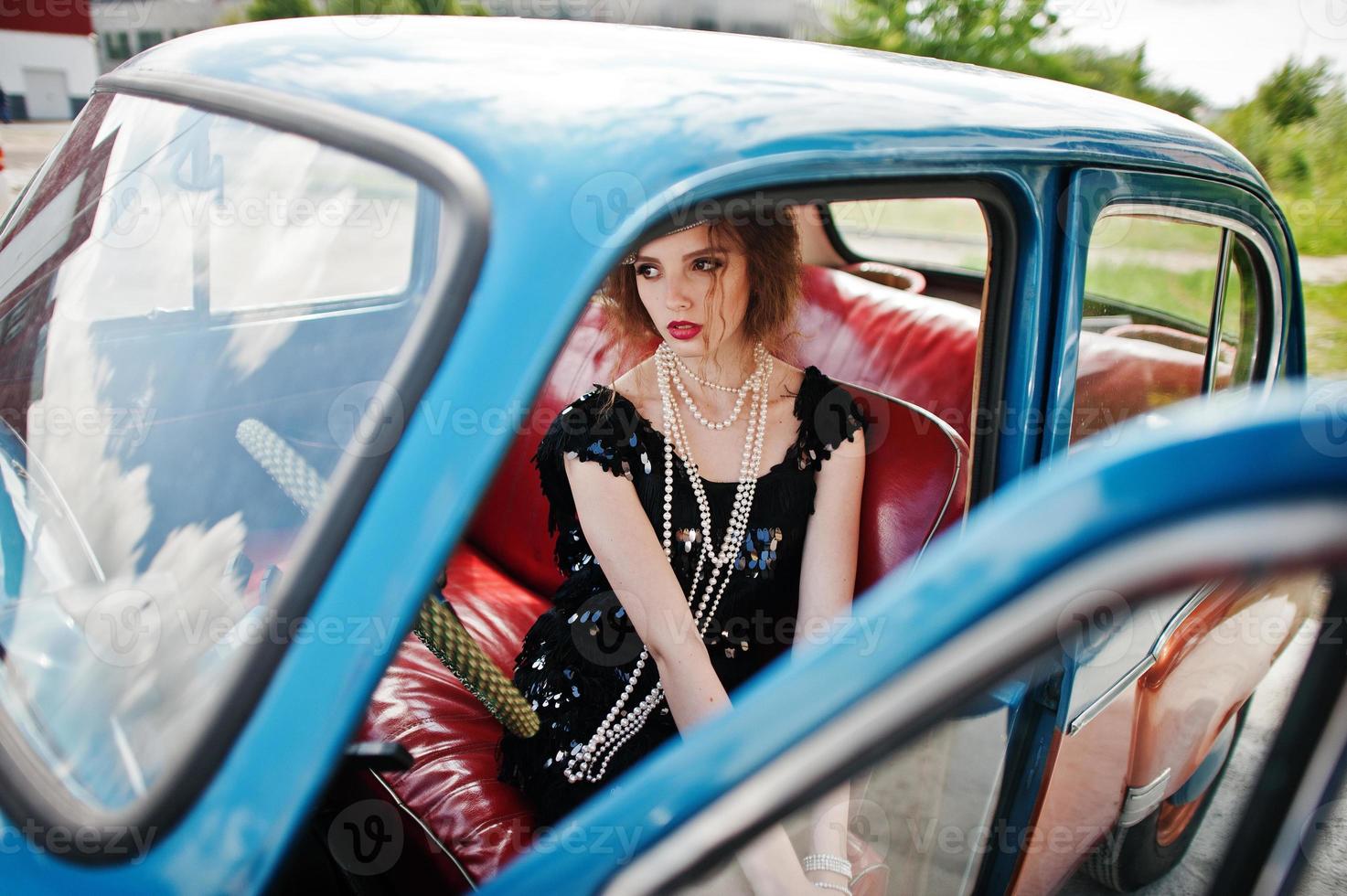 portrait d'un beau modèle de fille de mode bouclée avec un maquillage lumineux dans un style rétro assis sur une voiture d'époque photo