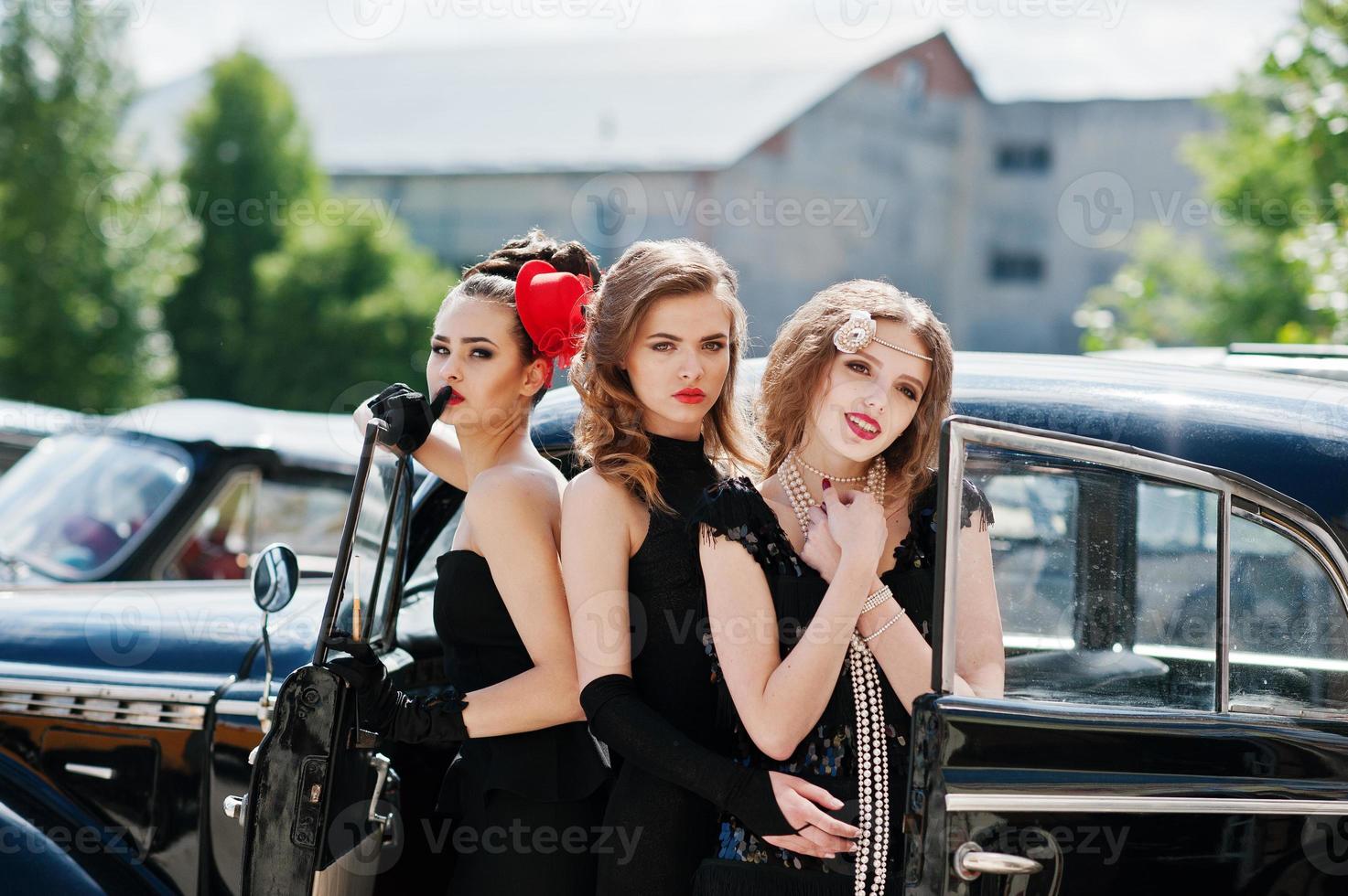 trois jeunes filles en robe de style rétro près de vieilles voitures vintage classiques. photo