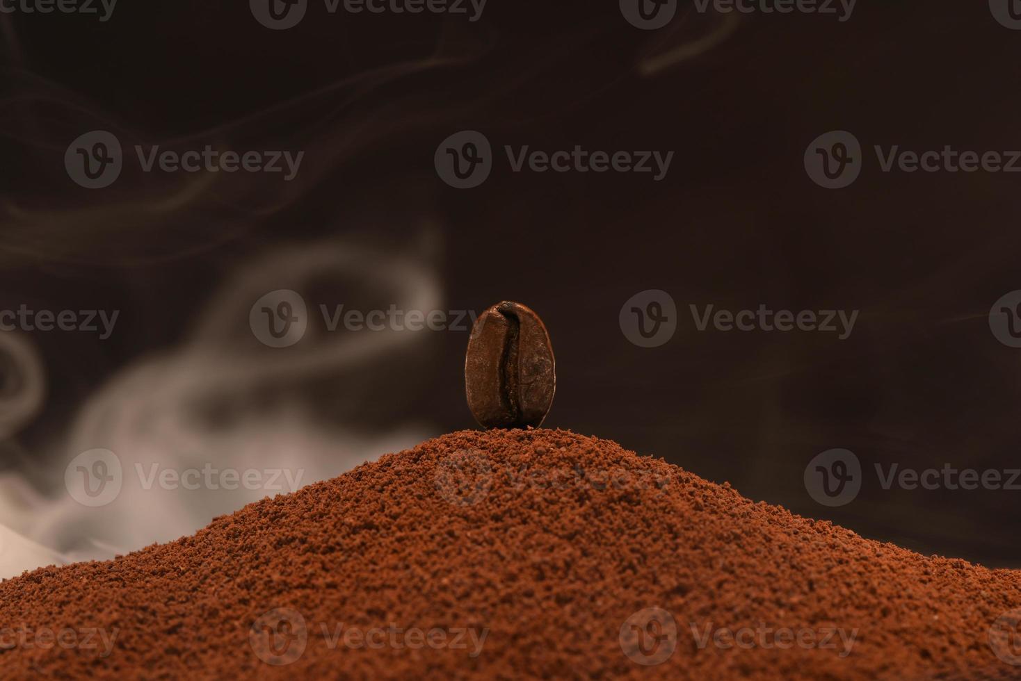 un grain de café fraîchement torréfié repose sur une dispersion de café moulu dans la fumée. photo