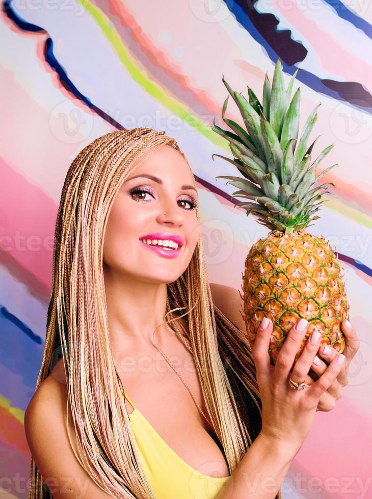 femme aux tresses africaines et aux ananas dans les mains en robe jaune photo