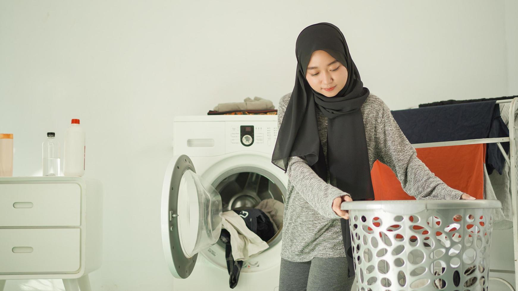 belle femme en hijab soulève le panier à linge à la maison photo