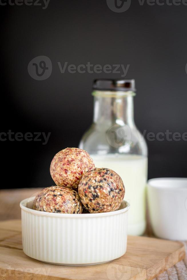 collation saine. boule d'énergie avec prune de date, sésame noir et blanc, chia et rasin dans un bol en céramique sur une table en bois. végétalien végétarien. photo