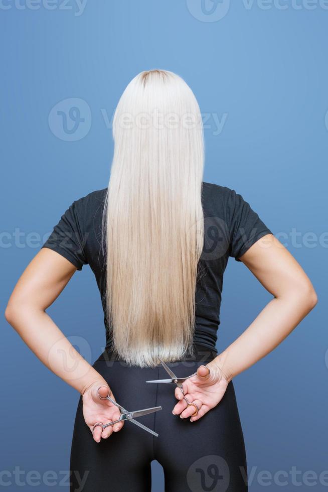 une femme avec une paire de ciseaux recule et coupe ses longs cheveux blonds. photo