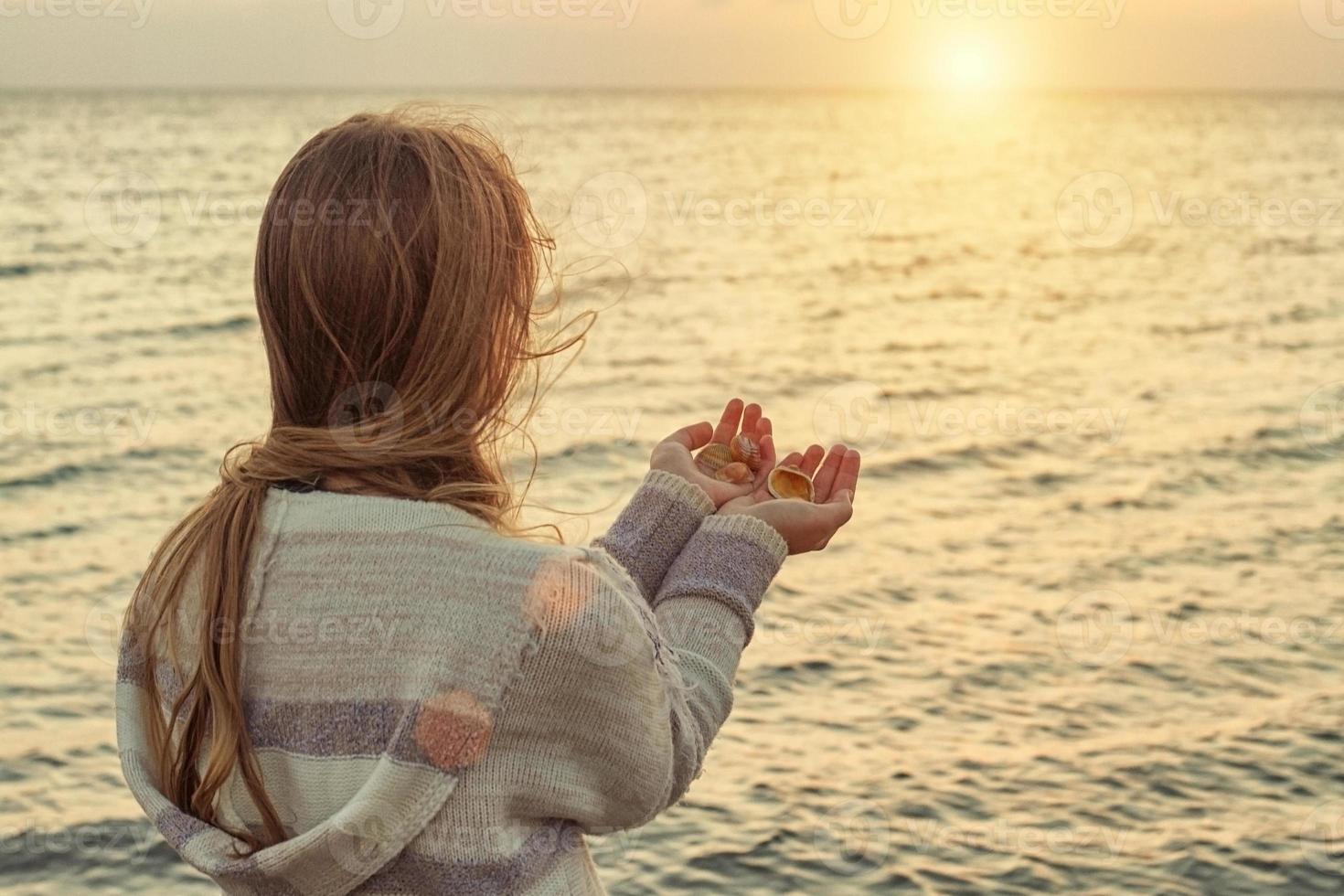 fille sur la plage tire sa main vers le soleil couchant photo