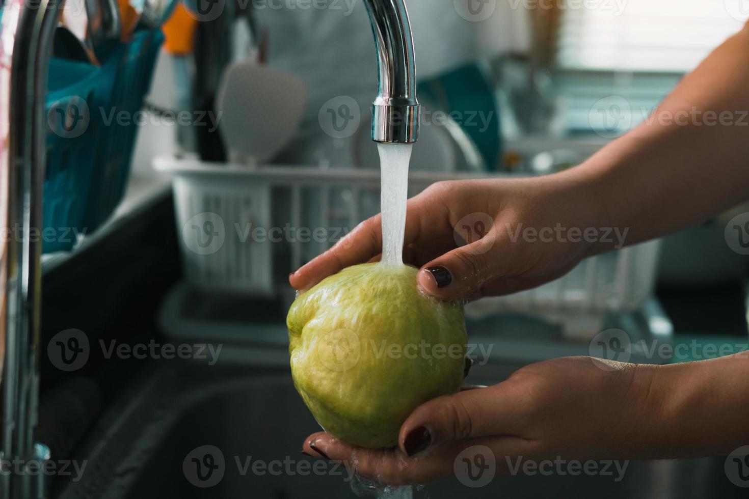 la main de la femme tient une goyave et se lave avec de l'eau au robinet de la cuisine à la maison. photo