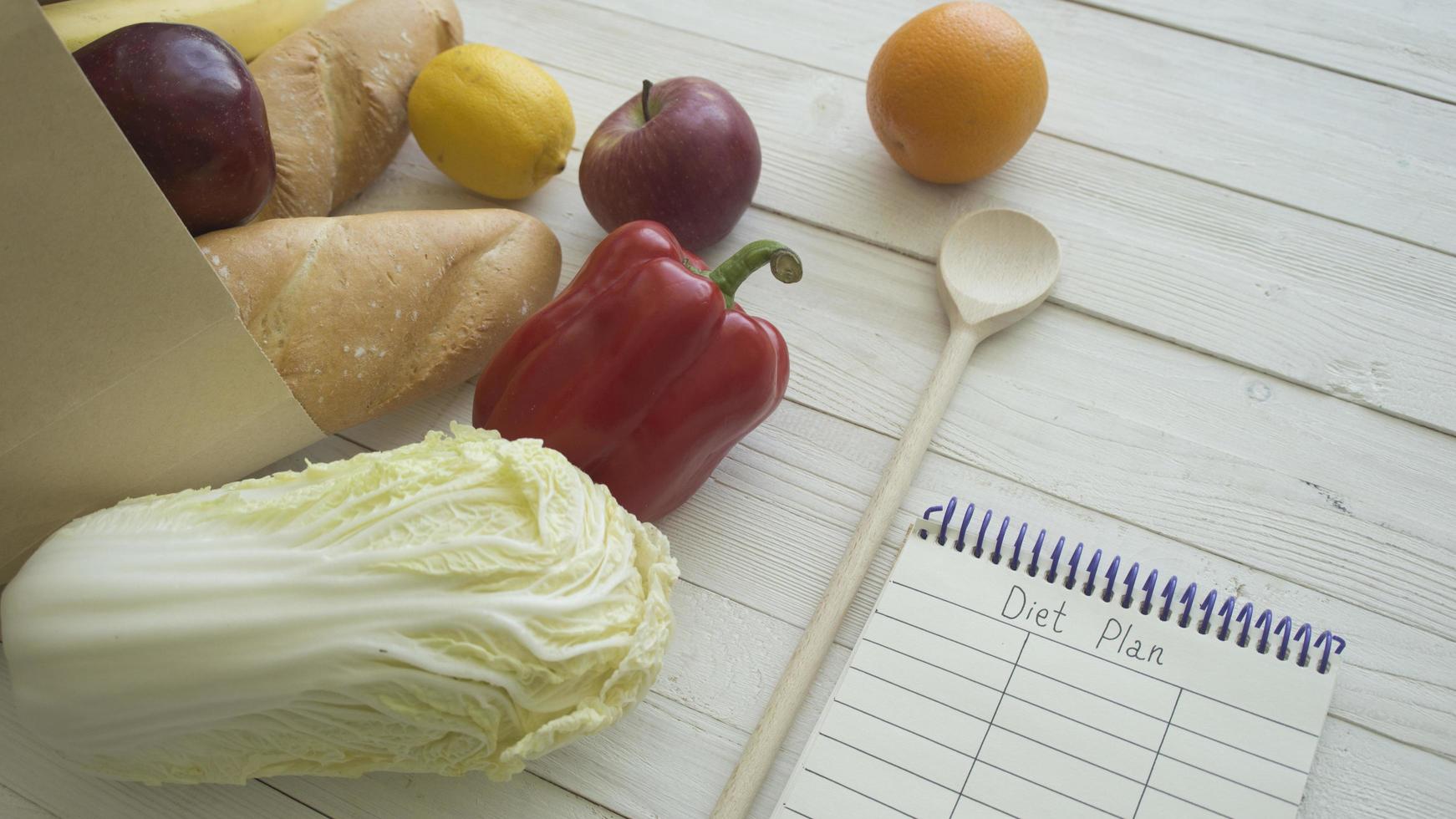 sac en papier plein de produits alimentaires avec petit cahier vierge sur table en bois, vue de dessus photo