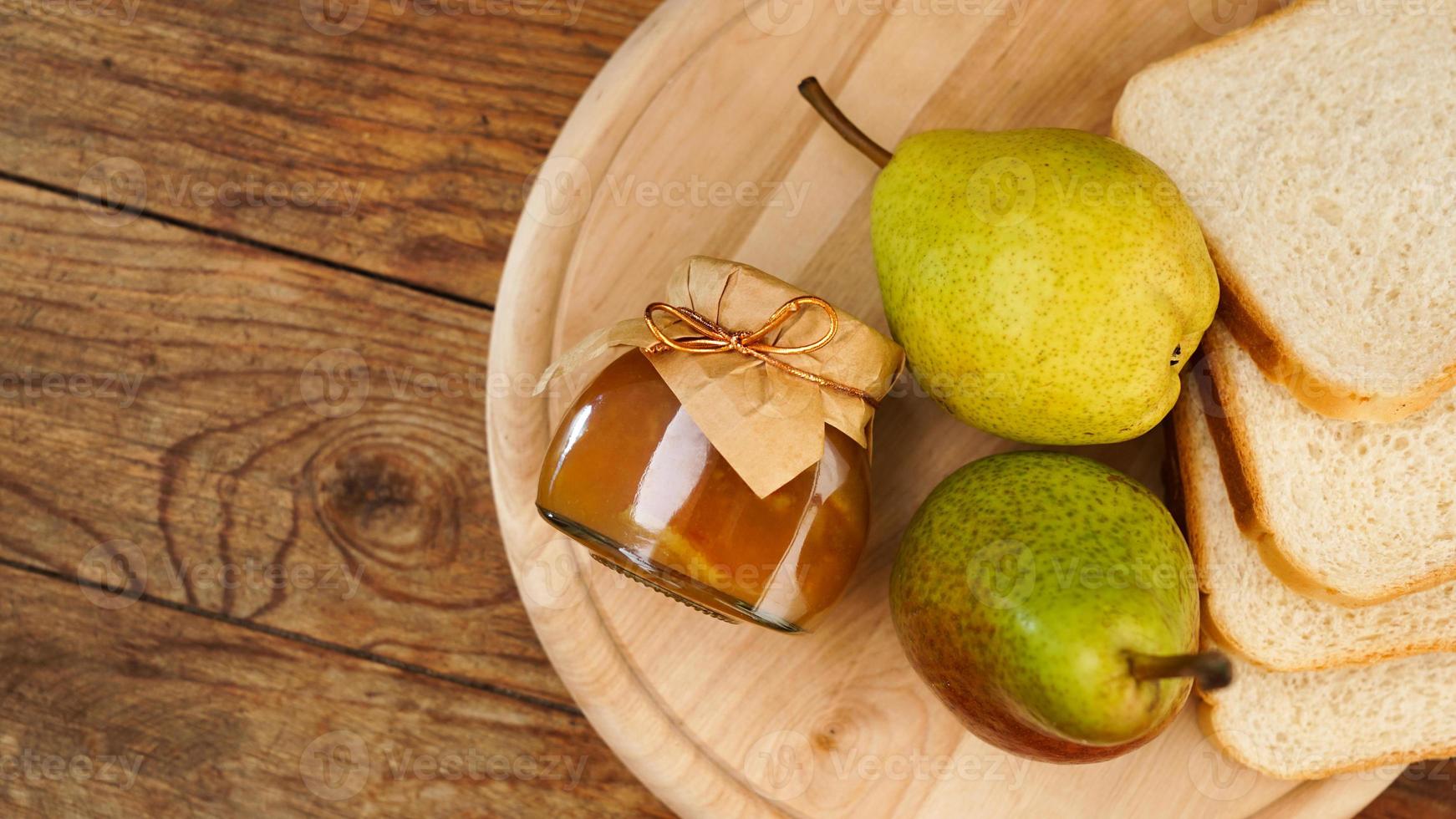 pot de confiture de poire savoureuse avec du pain et des poires fraîches sur une table en bois. vue de dessus photo
