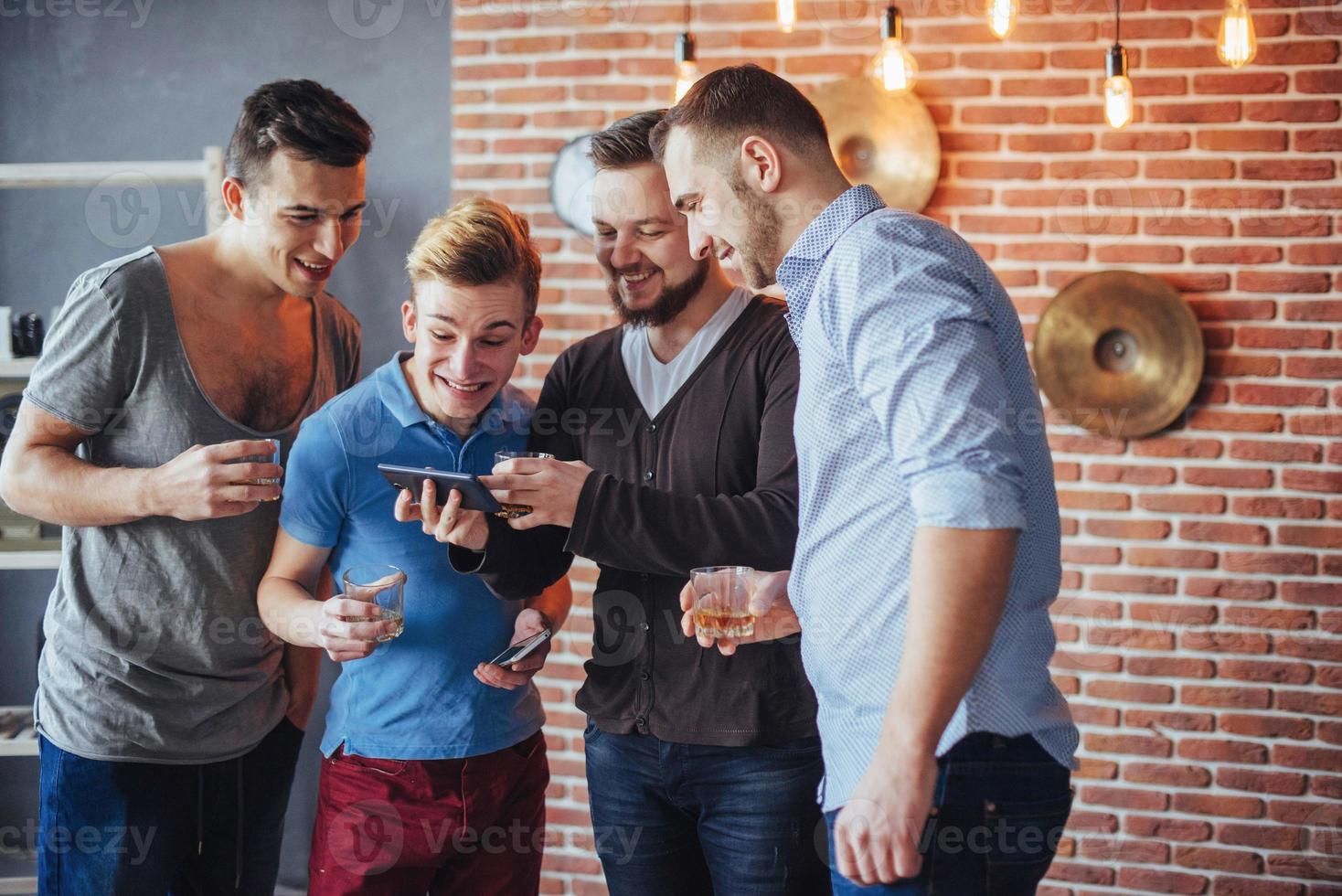 de vieux amis joyeux communiquent entre eux et regardent le téléphone, verres de whisky au pub. concept de mode de vie de divertissement. personnes connectées au wifi lors d'une réunion de table de bar photo