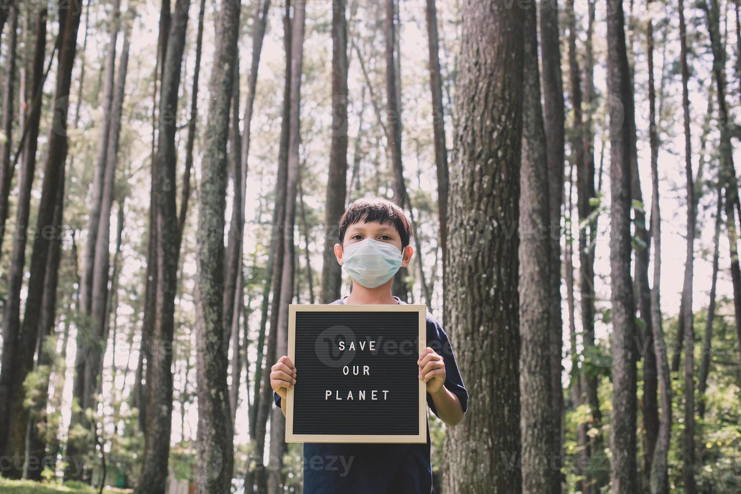 un garçon montrant une citation sur le tableau des lettres dit sauver notre planète avec la forêt en arrière-plan, le concept du jour de la terre photo