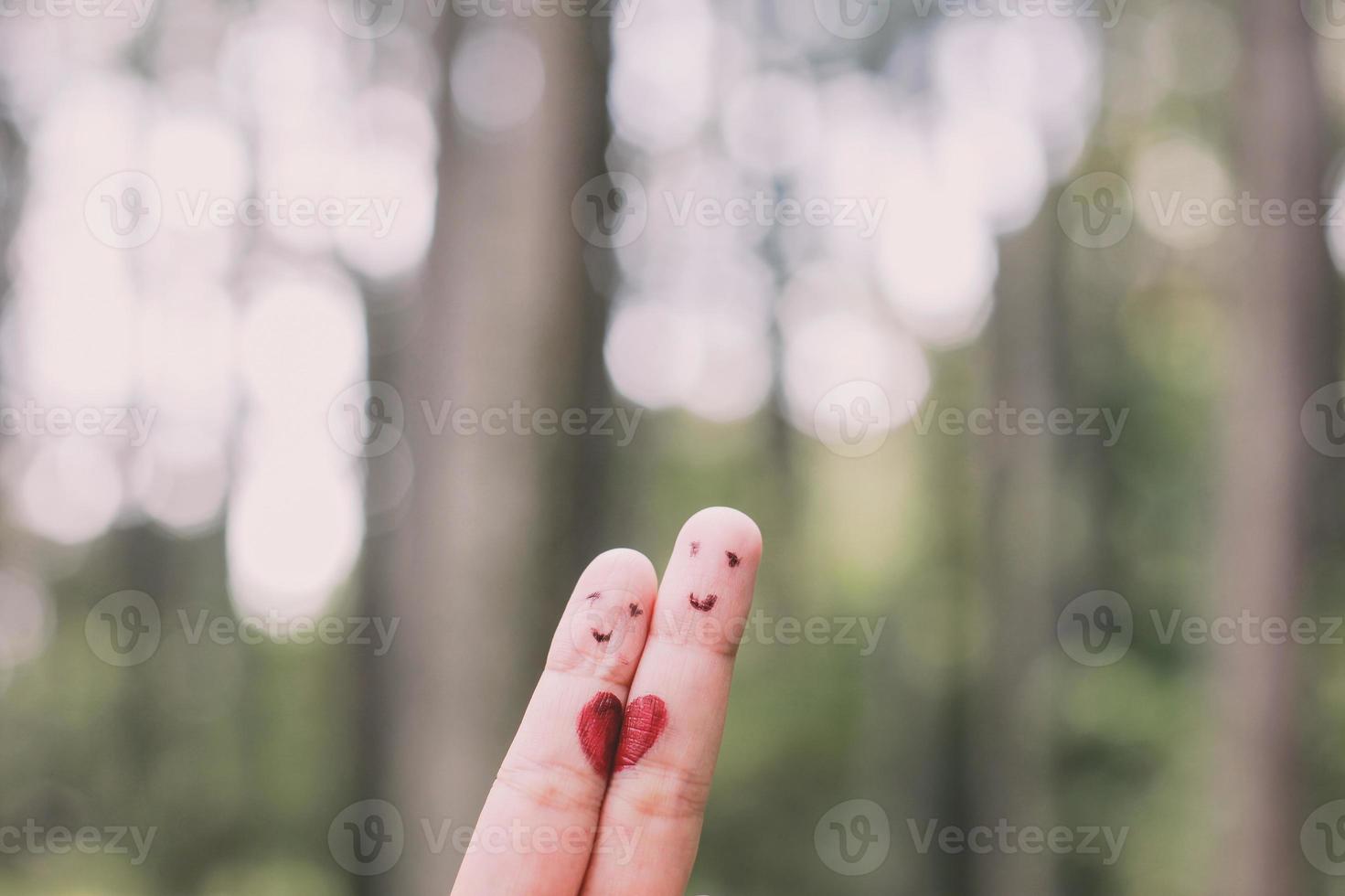 forme de coeur rouge sur deux doigts avec image de visage tout en souriant visage avec fond bokeh nature. espace de copie. heureux couple amoureux. photo