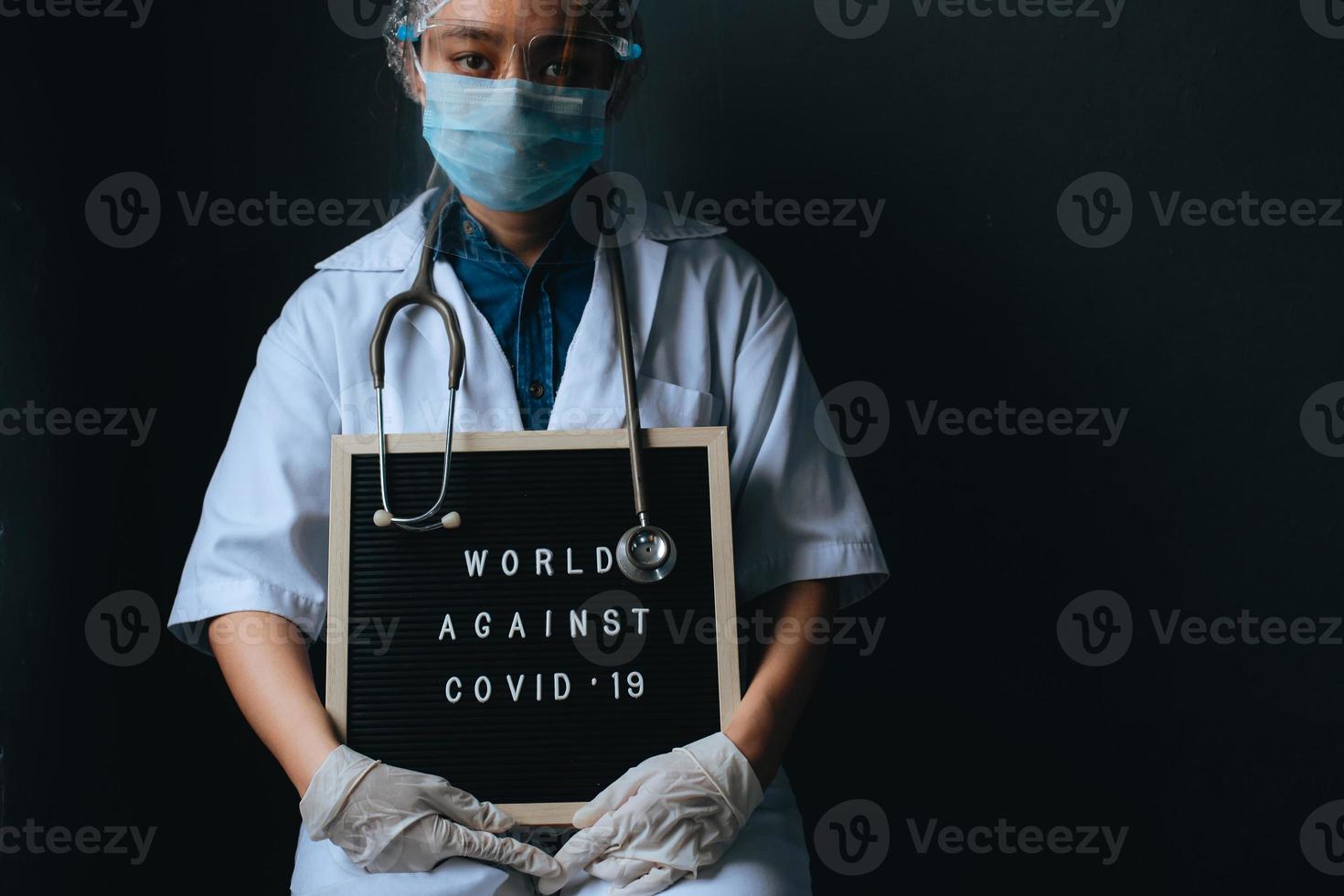 femme médecin avec citation sur le tableau des lettres dit monde contre covid 19 isolé sur fond noir. campagne contre le coronavirus avec espace de copie photo