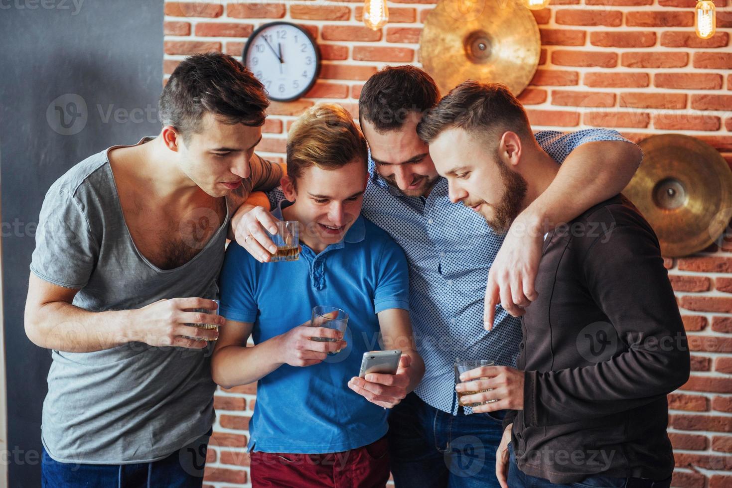 de vieux amis joyeux communiquent entre eux et regardent le téléphone, verres de whisky au pub. concept de mode de vie de divertissement. personnes connectées au wifi lors d'une réunion de table de bar photo