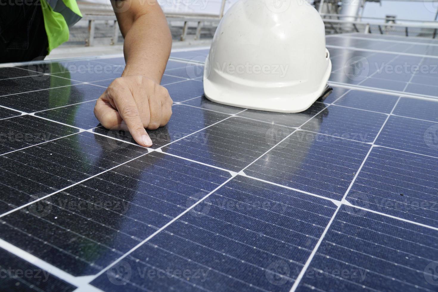 un ingénieur électricien portant un chapeau blanc vérifie. propreté des panneaux solaires sur le toit de l'immeuble. photo