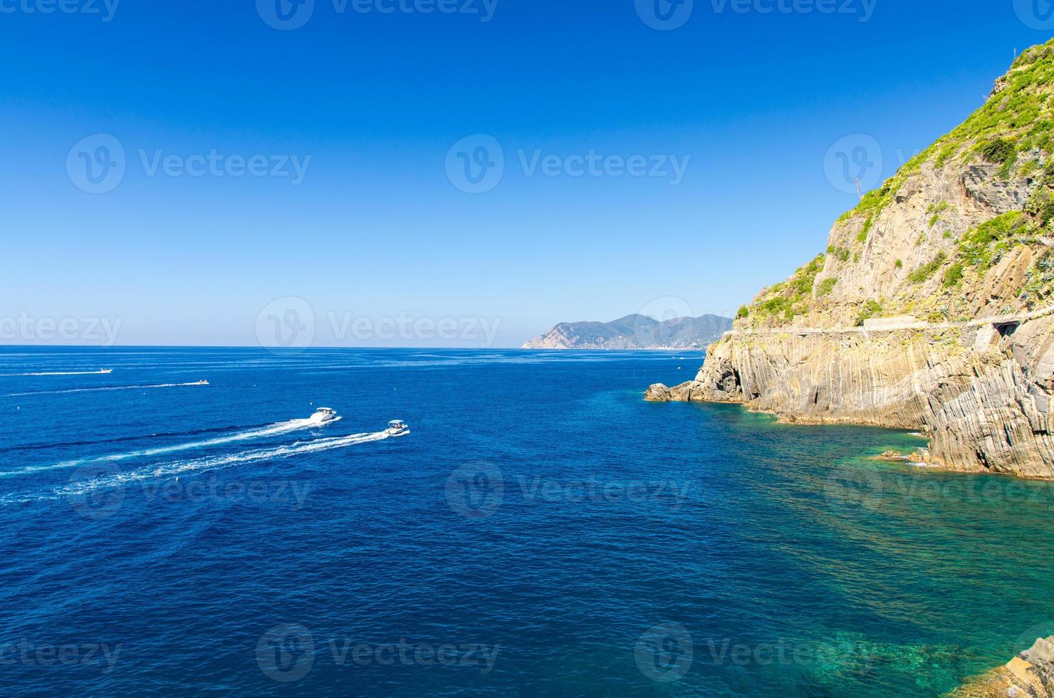 deux yachts bateaux naviguent sur l'eau de la mer ligurienne et méditerranéenne près du littoral de la riviera di levante du parc national côte des cinque terre avec espace de copie de ciel bleu, village de riomaggiore, ligurie, italie photo