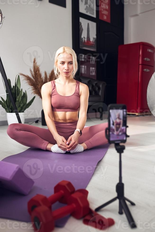 la jeune belle blonde prend soin de son corps à la maison pendant la quarantaine. elle forme les gens en ligne via son téléphone portable photo