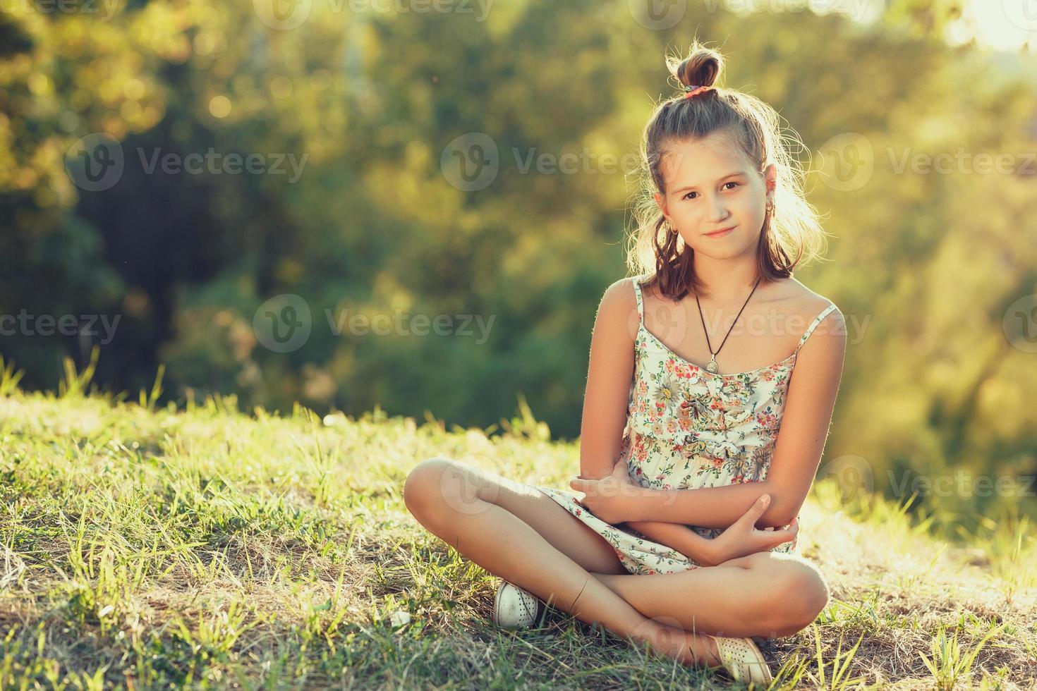 belle fille est assise sur l'herbe et regarde la caméra. vêtu d'un sarafan photo