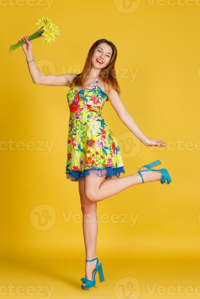jeune femme contre le mur jaune avec des fleurs à la main photo