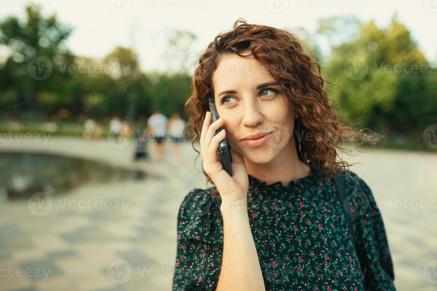 portraits d'une charmante fille rousse avec un joli visage. la fille parle gentiment avec quelqu'un au téléphone. elle a une bonne humeur et un doux sourire photo