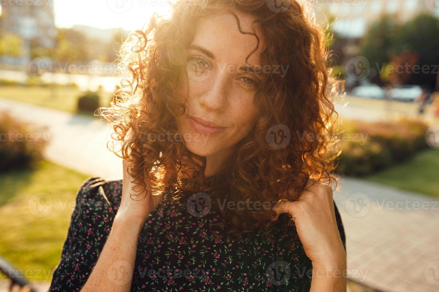 charmante fille rousse bouclée avec des taches de rousseur en robe pose pour la caméra dans le centre-ville montrant différentes émotions faciales photo