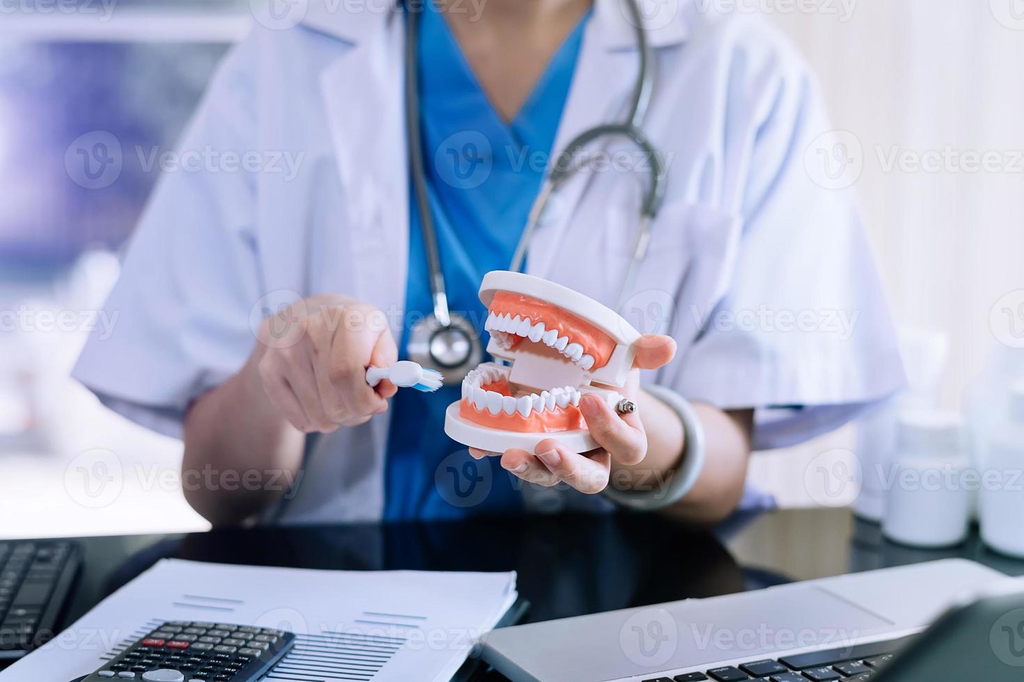 dentiste concentré assis à table avec des échantillons de mâchoire modèle de dent et travaillant avec tablette et ordinateur portable dans un cabinet dentaire photo