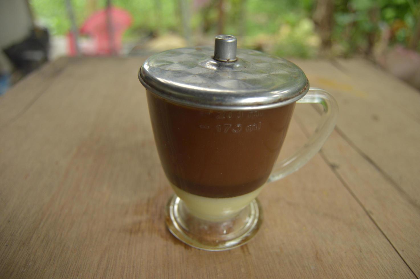 servir du café avec un verre transparent et du lait concentré en dessous. fond en bois extérieur. photo