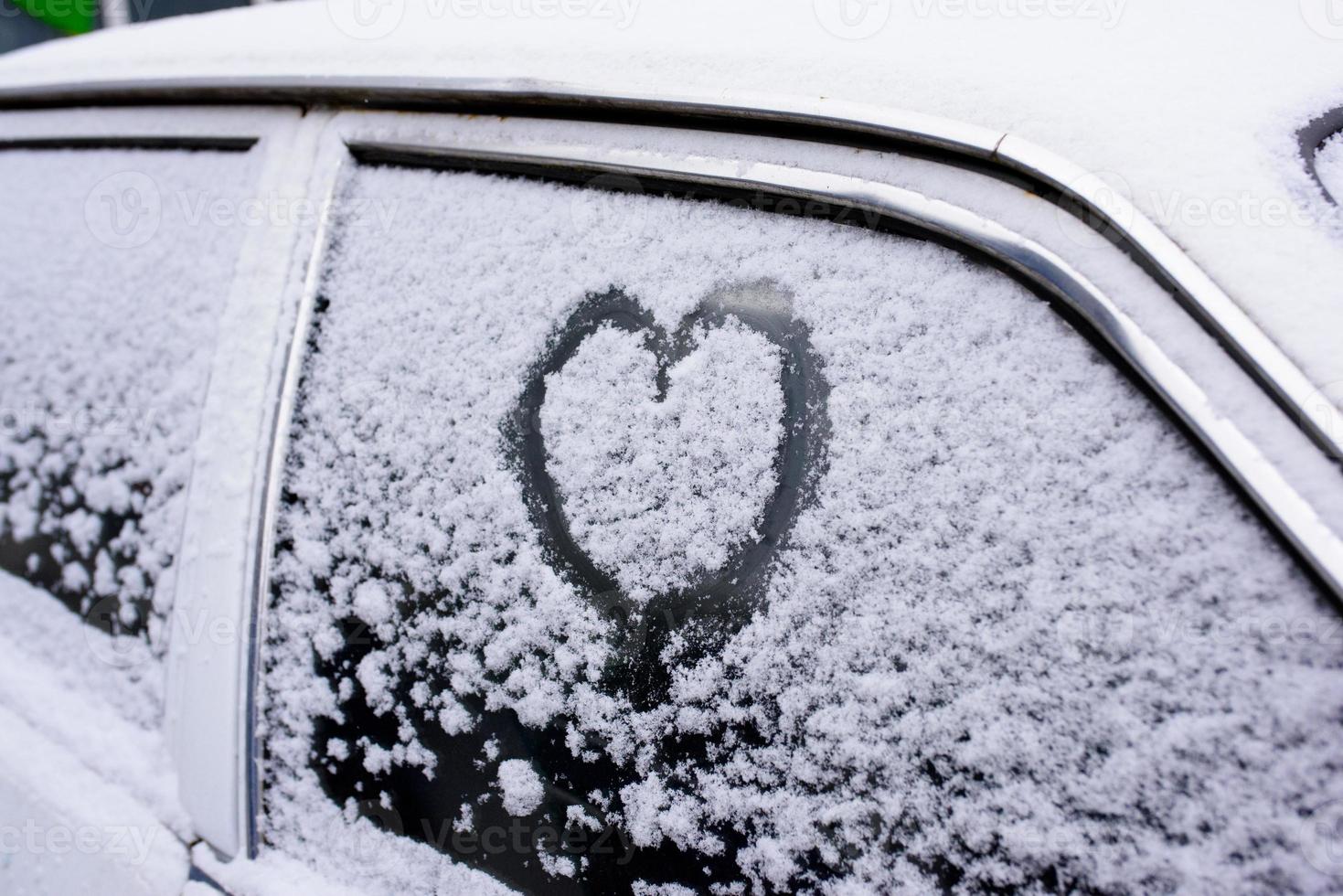 coeur dessiné sur un pare-brise de voiture recouvert de neige fraîche de noël photo