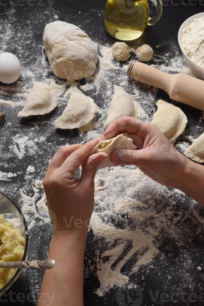 femme sculpte des boulettes avec des pommes de terre à la main sur un fond noir. tiré de l'angle supérieur. cuisine folklorique ukrainienne. photo