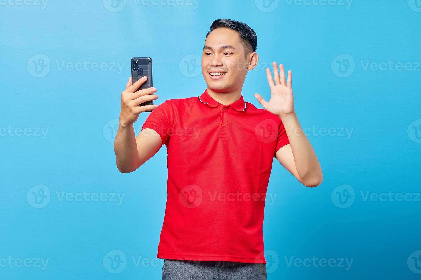 portrait d'un jeune homme asiatique joyeux faisant un appel vidéo et agitant la caméra du smartphone isolé sur fond bleu photo