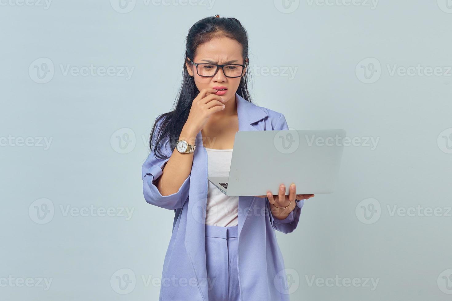 portrait d'une jeune femme asiatique effrayée debout à l'aide d'un ordinateur portable et de ronger les ongles isolés sur fond blanc photo