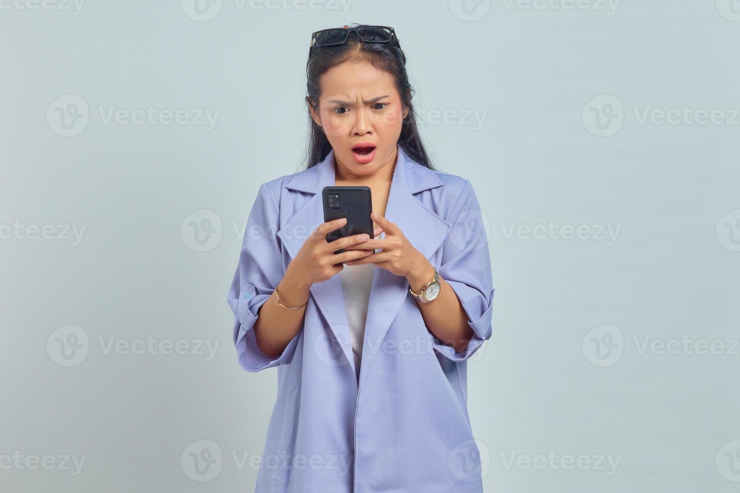 portrait d'une jeune femme asiatique surprise à l'aide d'un téléphone portable isolé sur fond blanc photo