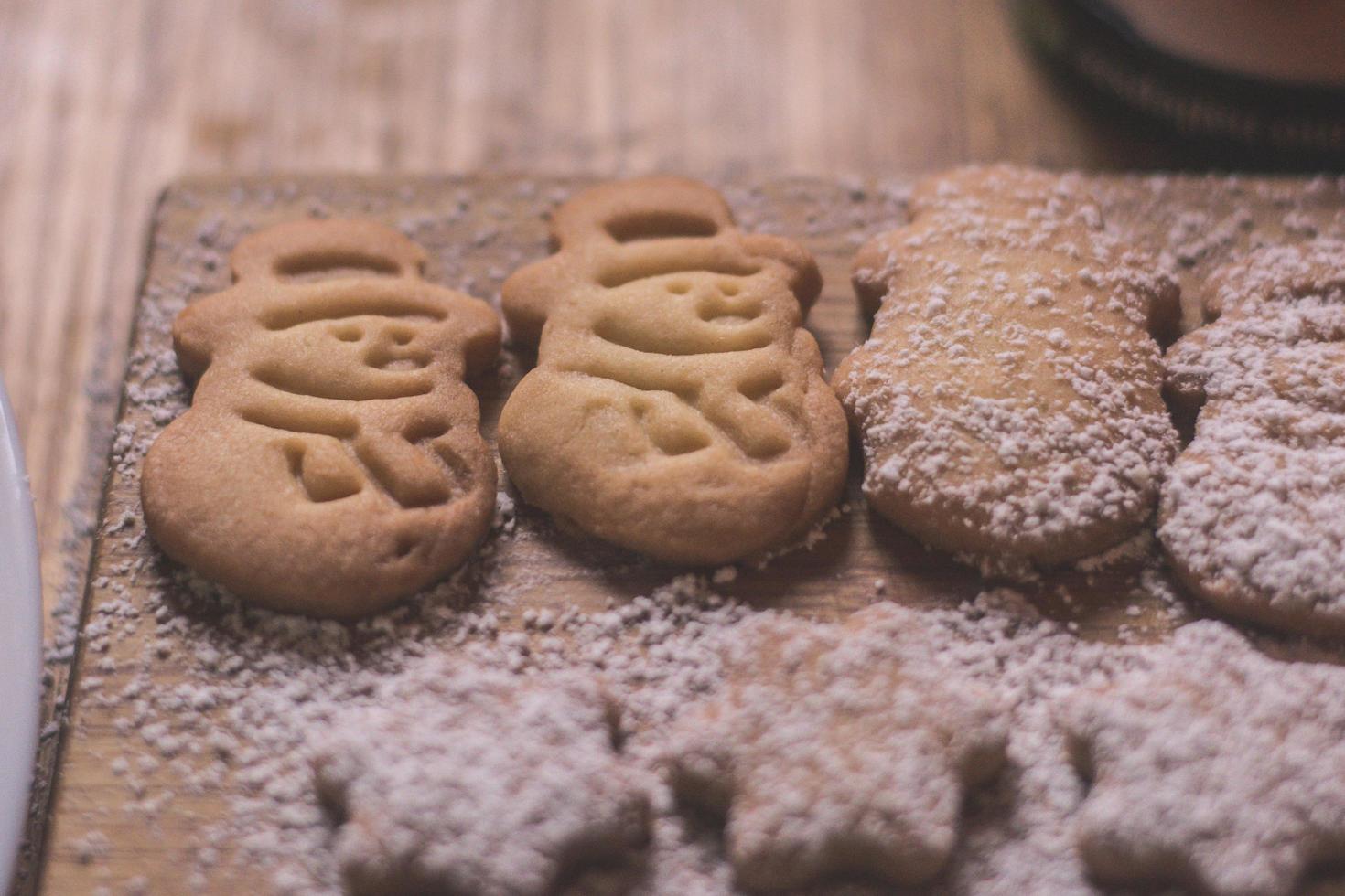 Biscuits en poudre fraîchement cuits en forme de bonhomme de neige allongés sur une planche à découper. photo