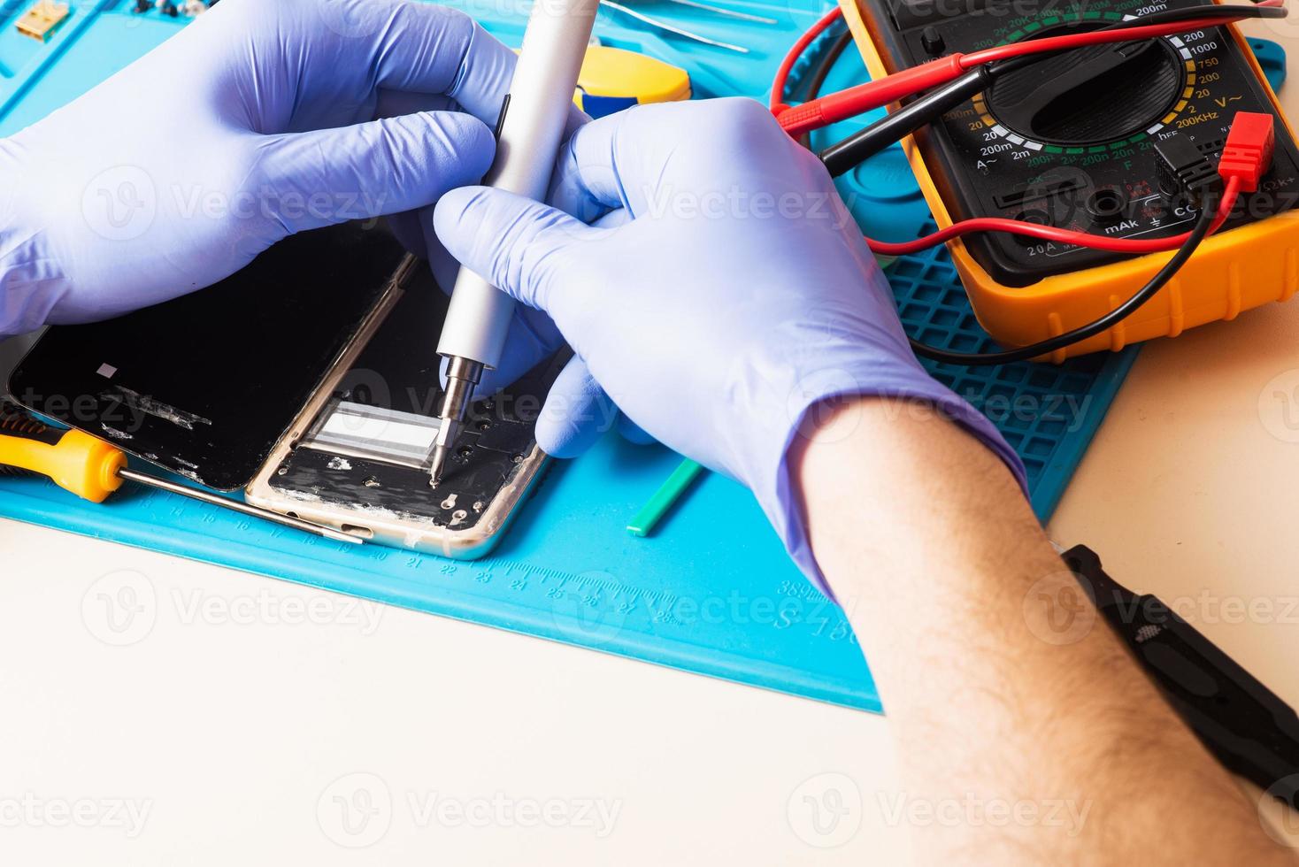 artisan en gants de caoutchouc répare ou entretient un téléphone portable sur un tapis en caoutchouc spécial pour réparation. vue de l'intérieur photo