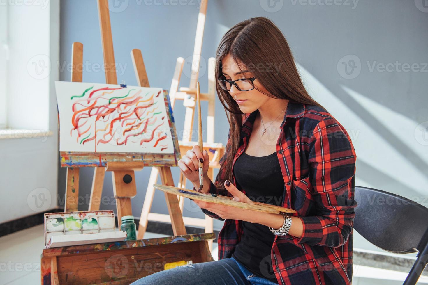 Creative pensive peintre fille peint une image colorée sur toile avec des couleurs à l'huile en atelier photo