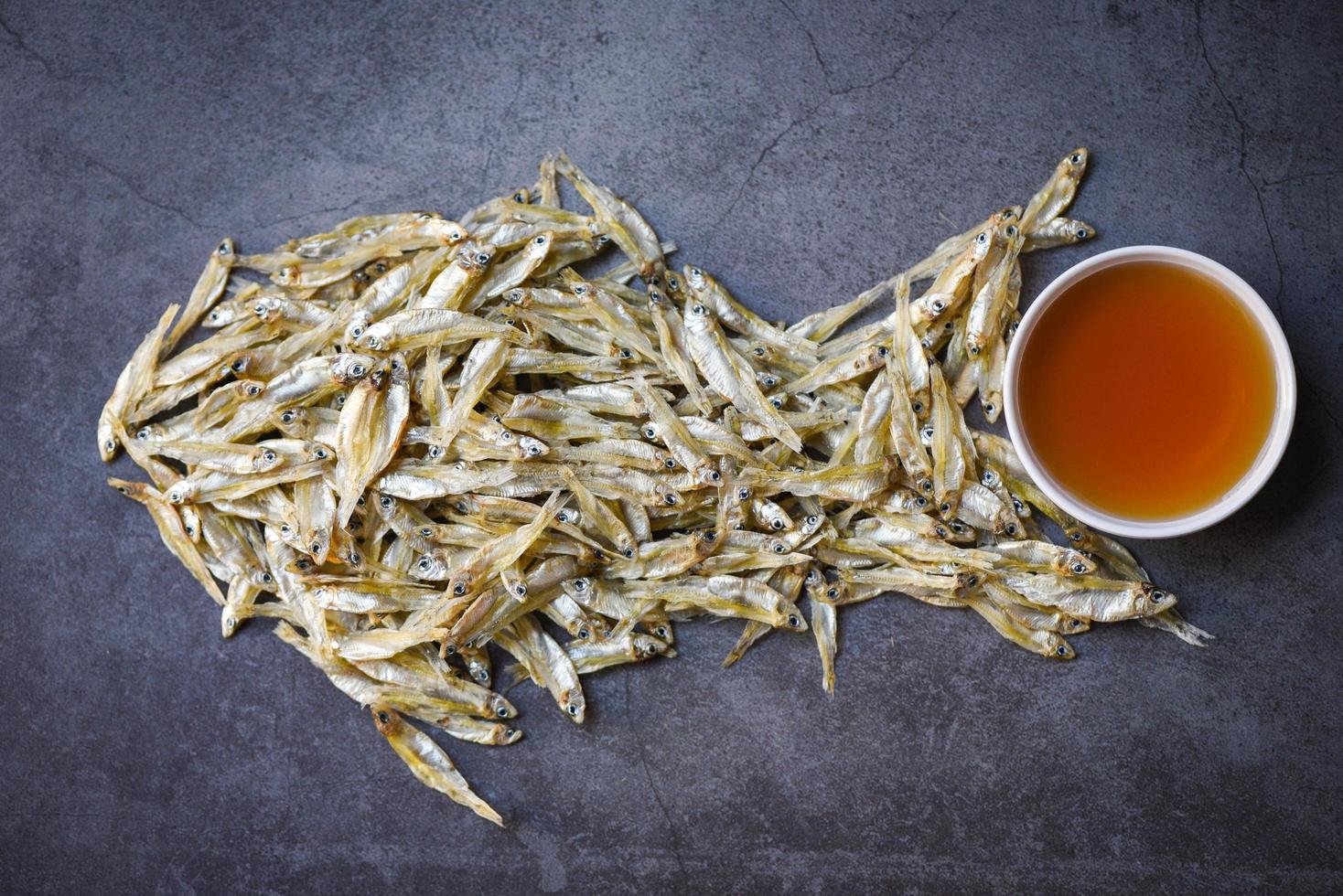 sauce de poisson sur bol blanc et petit poisson séché sur fond sombre, sauce de poisson obtenue à partir de poisson de fermentation ou de petit animal aquatique, aliments fermentés photo